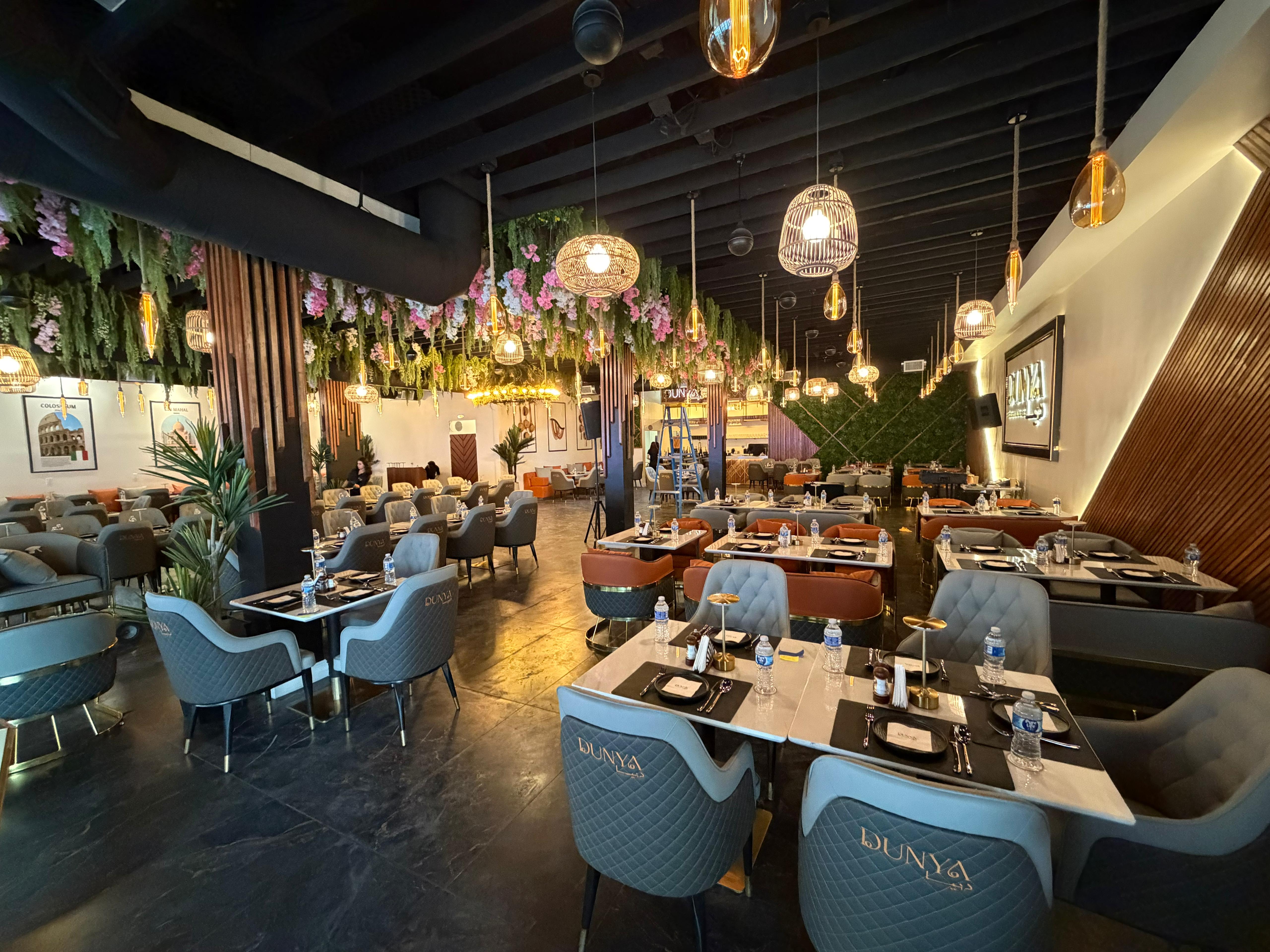 Dunya Lounge interior dining room with branded chairs, hanging pendant lights, lush greenery and warm ambient atmosphere